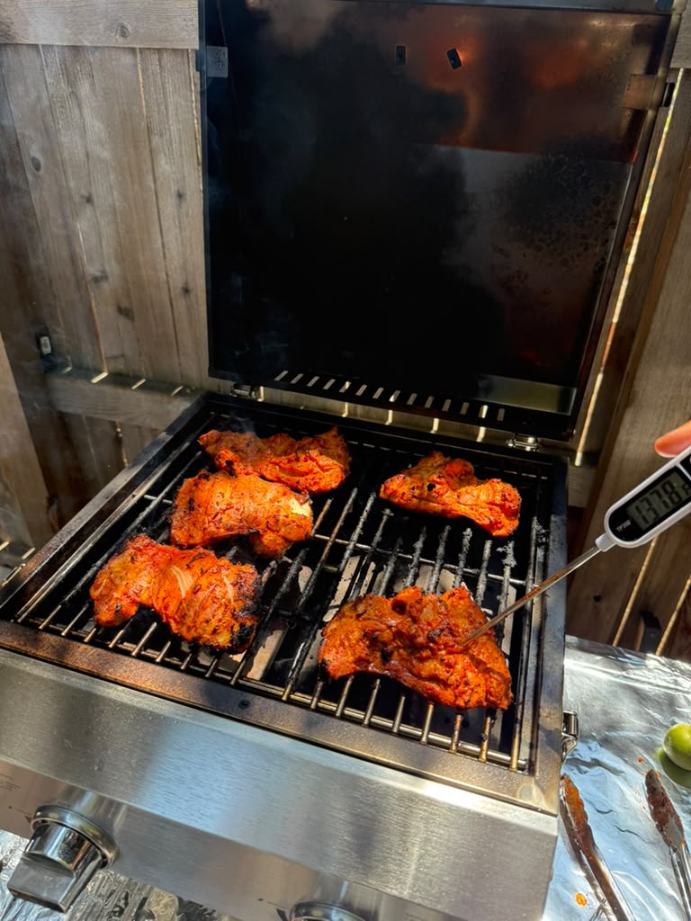 Tandoori chicken thighs coming off the coals, edges charred and glossy